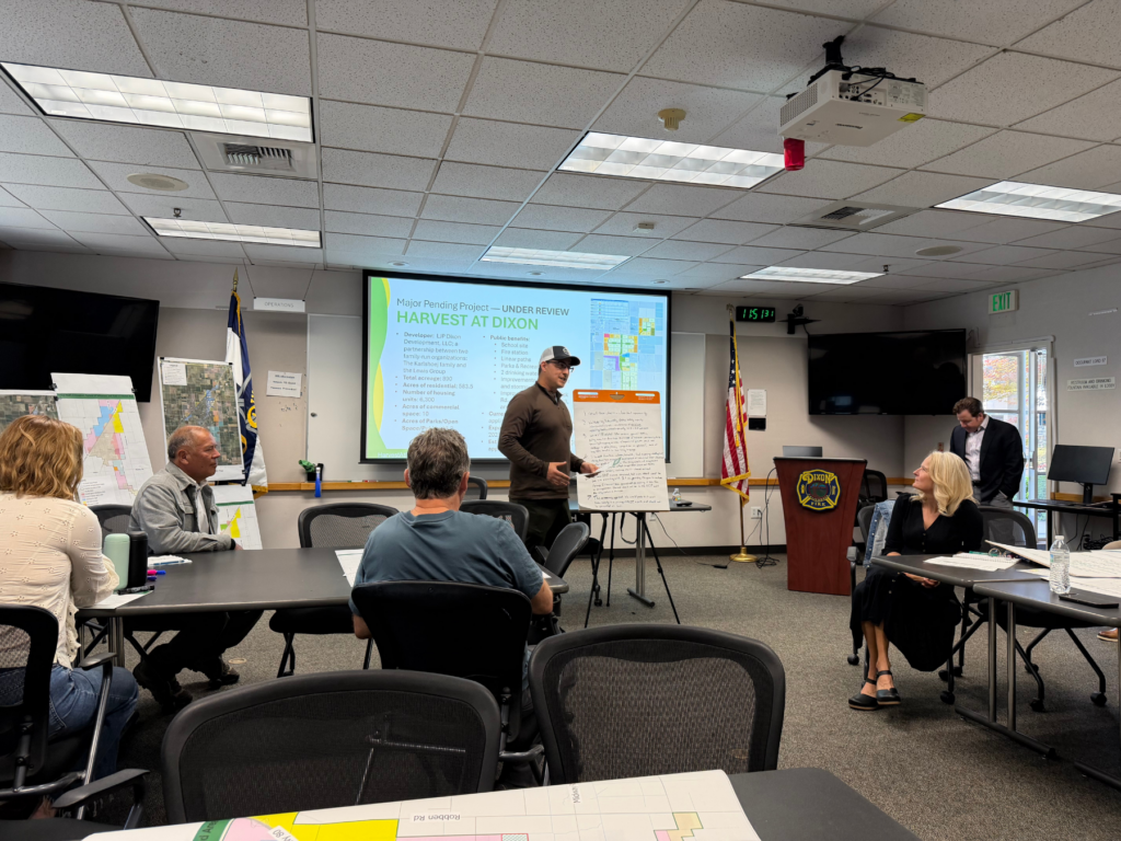 A presenter leads a discussion using a flip chart for a seated audience at the community workshop.