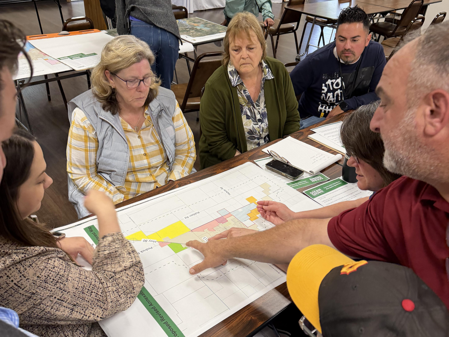 A group of people gathered around a table, intently discussing a colorful map.