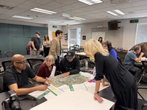 A group of people gather around a table in a meeting room to discuss maps and documents during a Dixon Grown workshop.